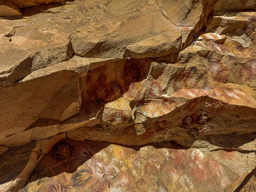 Decenas de manos pintadas en ocre, rojo y blanco sobre la pared de roca