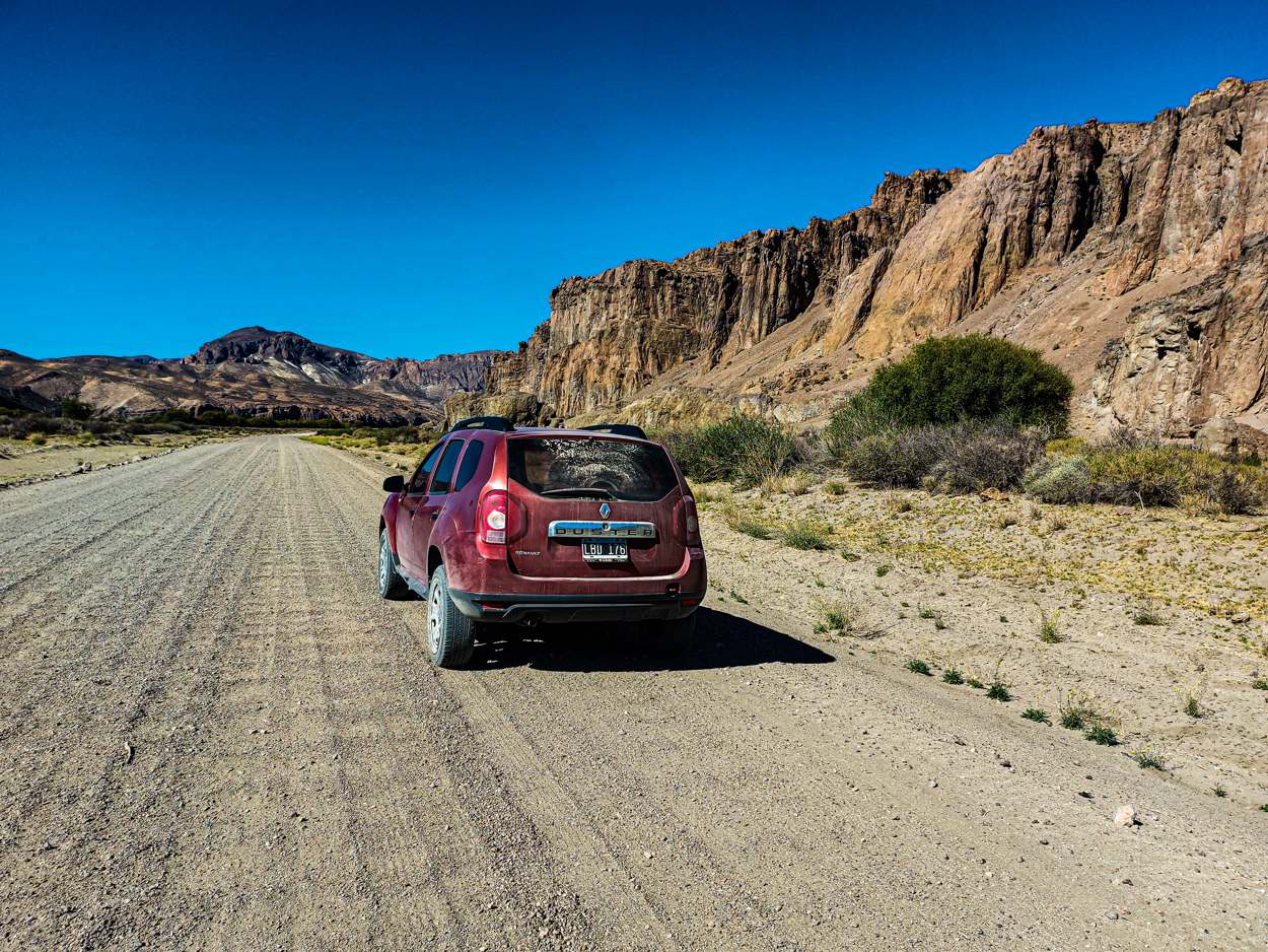 La camioneta roja avanzando por un camino de ripio junto a un paredón
