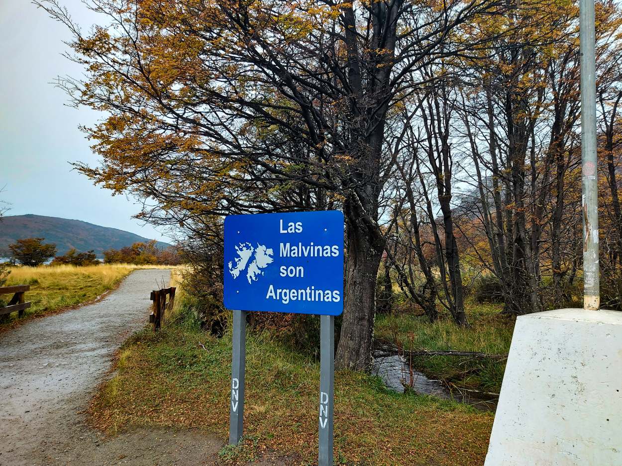 Cartel de ruta azul junto a un sendero, entre árboles de otoño