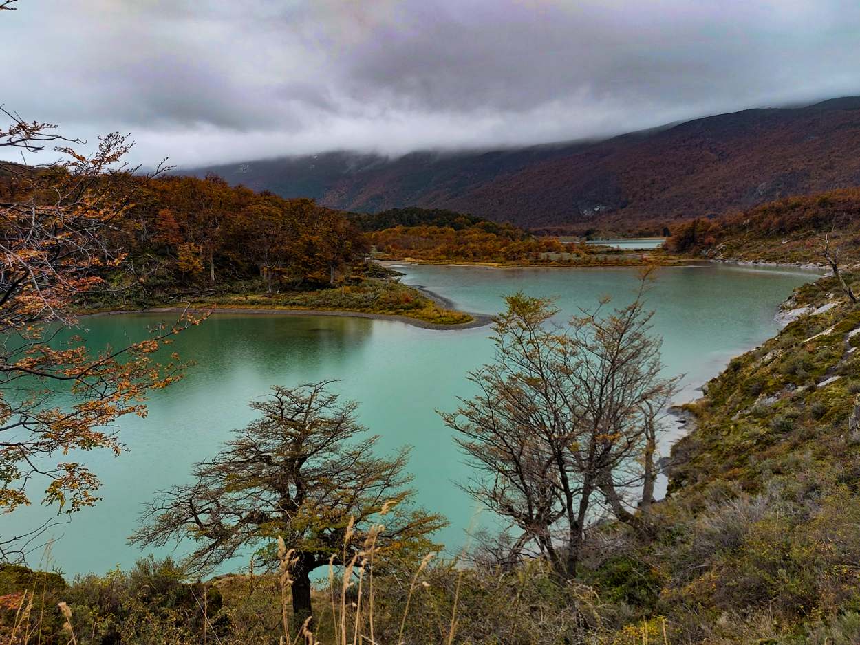 Laguna de agua verde esmeralda rodeada de bosque otoñal, con nubes bajas sobre el cerro