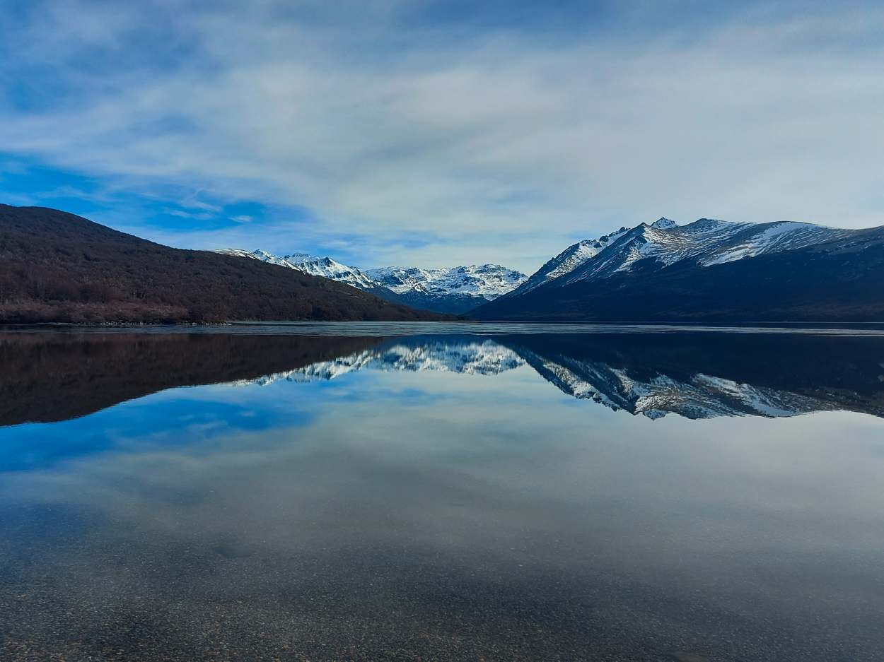 Un lago en calma que refleja las montañas nevadas como un espejo